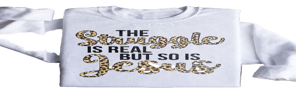White sweatshirt with 'The Struggle is Real but So is Jesus' text on a wooden surface